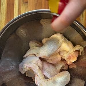 raw chicken wings in a silver bowl, with someone spraying oil on top