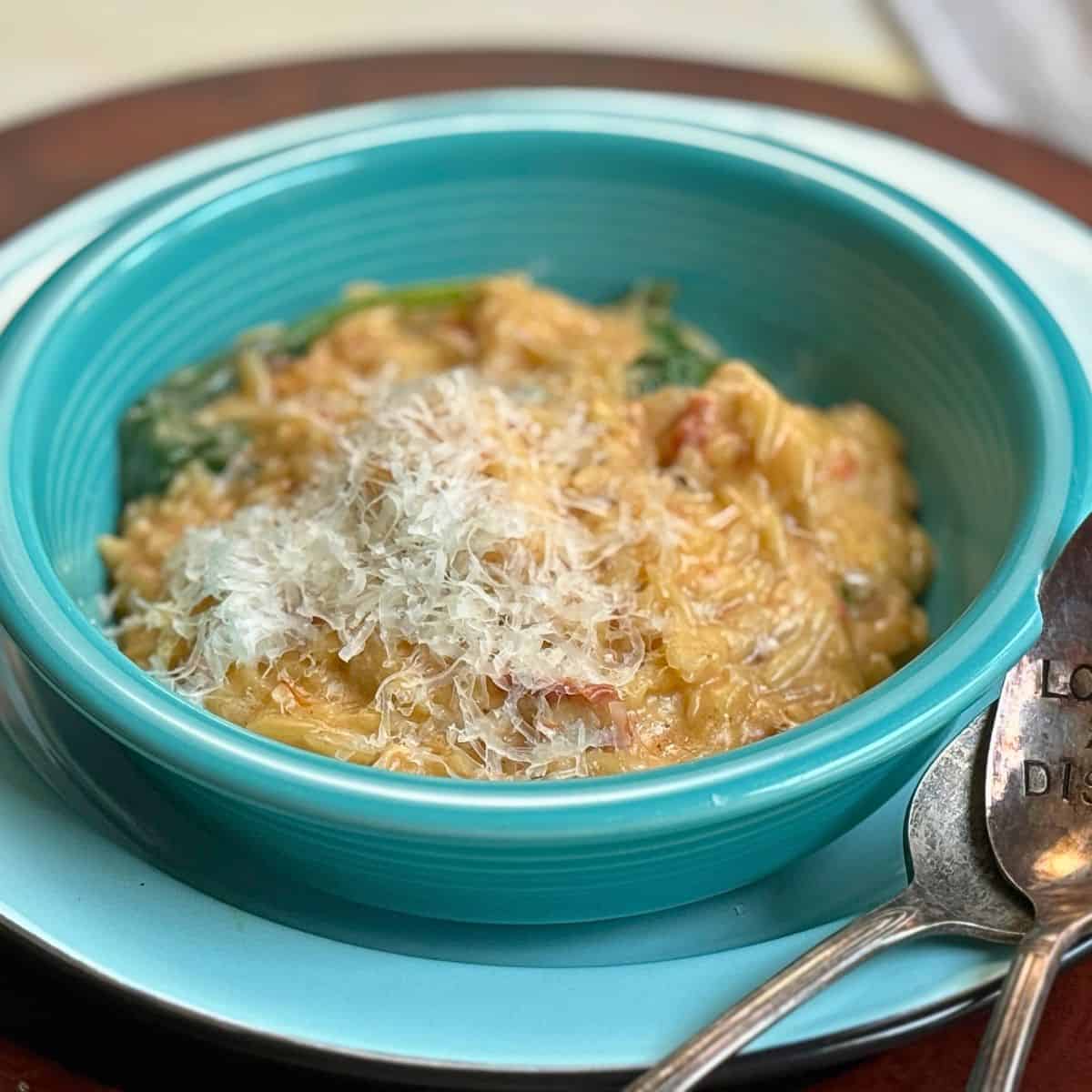 Orzo in a creamy sauce on a blue plate with spoons and parmesan cheese on top