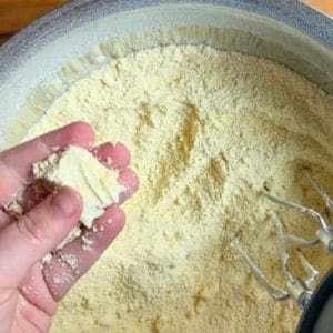 hand holding a clump of butter and cake mix mixture over a silver bowl