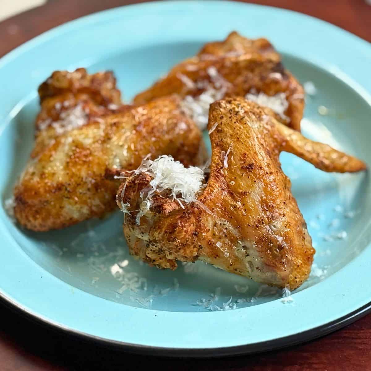 Three chicken wings on a blue plate with freshly grated parmesan cheese on top