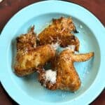 Three chicken wings on a light blue plate with a wooden background.