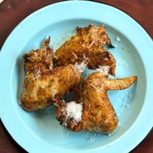 Three chicken wings on a light blue plate with a wooden background.