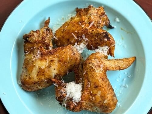 Three chicken wings on a light blue plate with a wooden background.