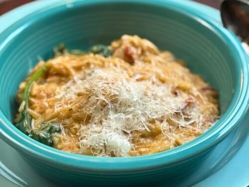cheesey chicken and orzo in a blue dish with spinach and a spoon