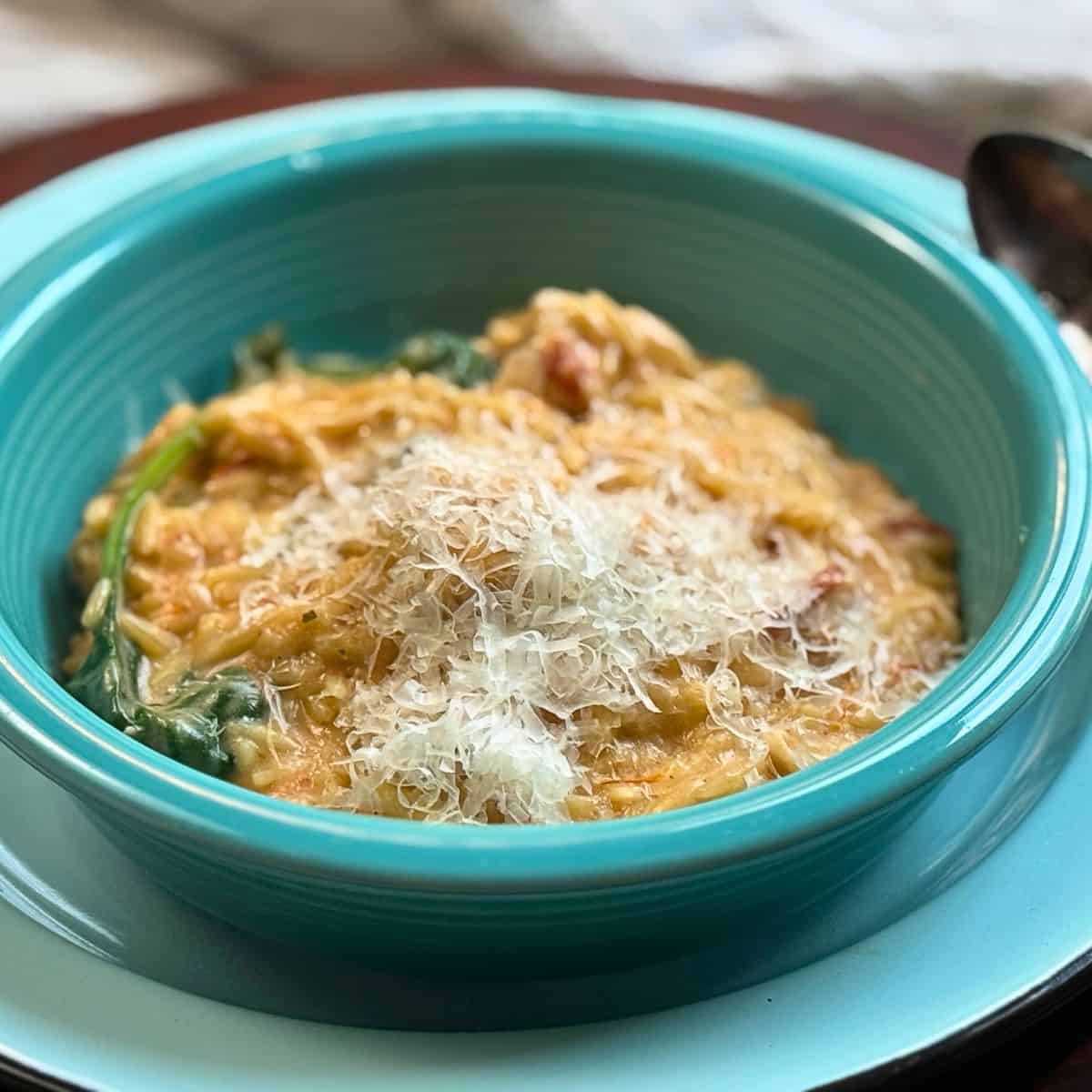 cheesey chicken and orzo in a blue dish with spinach and a spoon