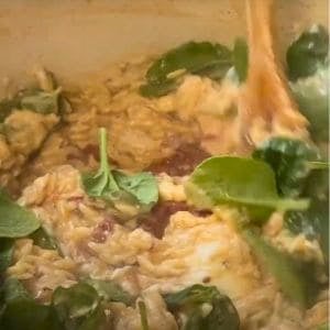 spinach added to cooked orzo and being mixed with a wooden spoon.