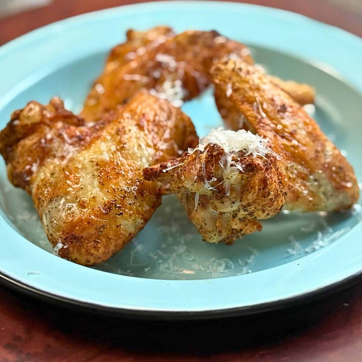 Three chicken wings on a blue plate with parmesan cheese on top