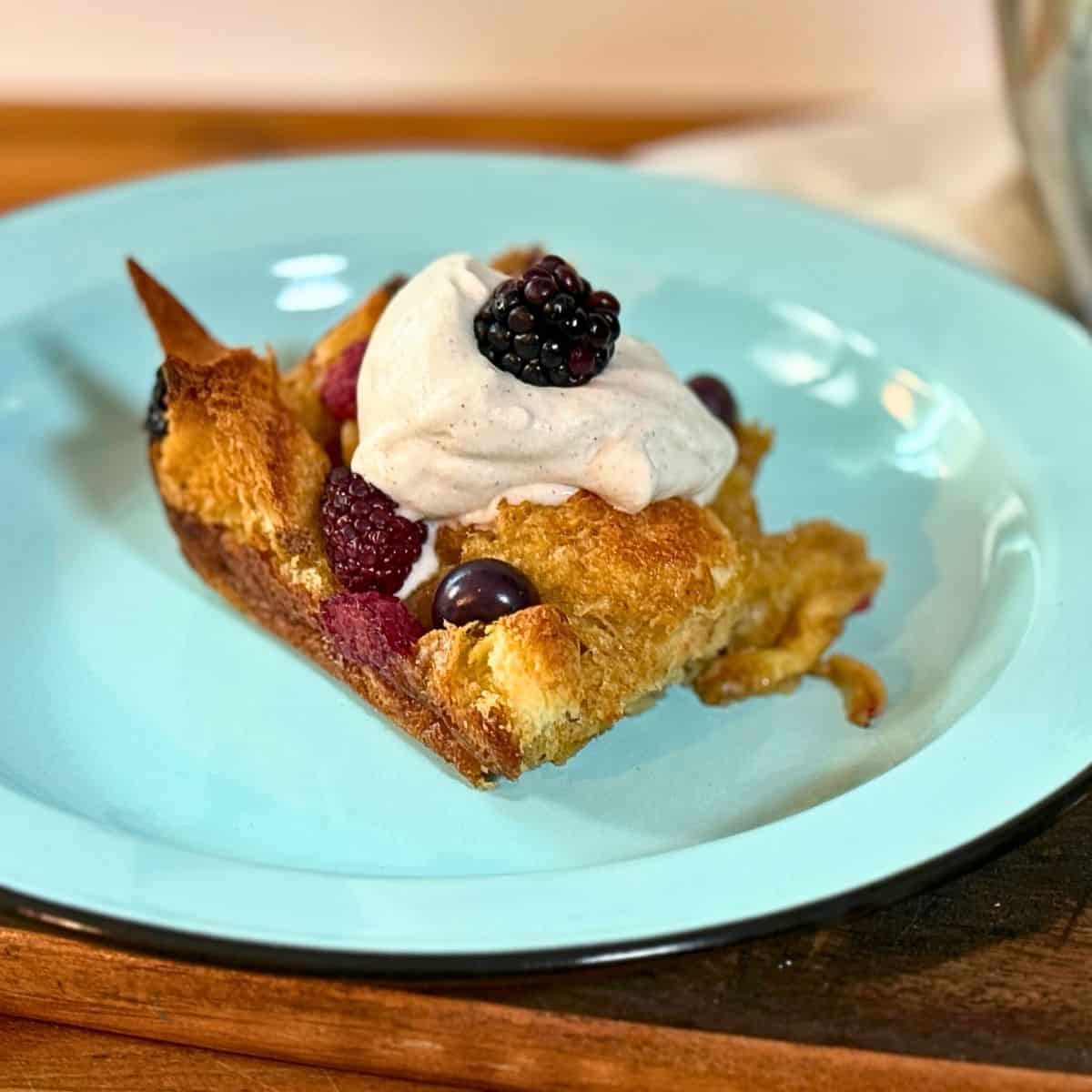 slice of french toast on a blue plate with berries and whipped cream