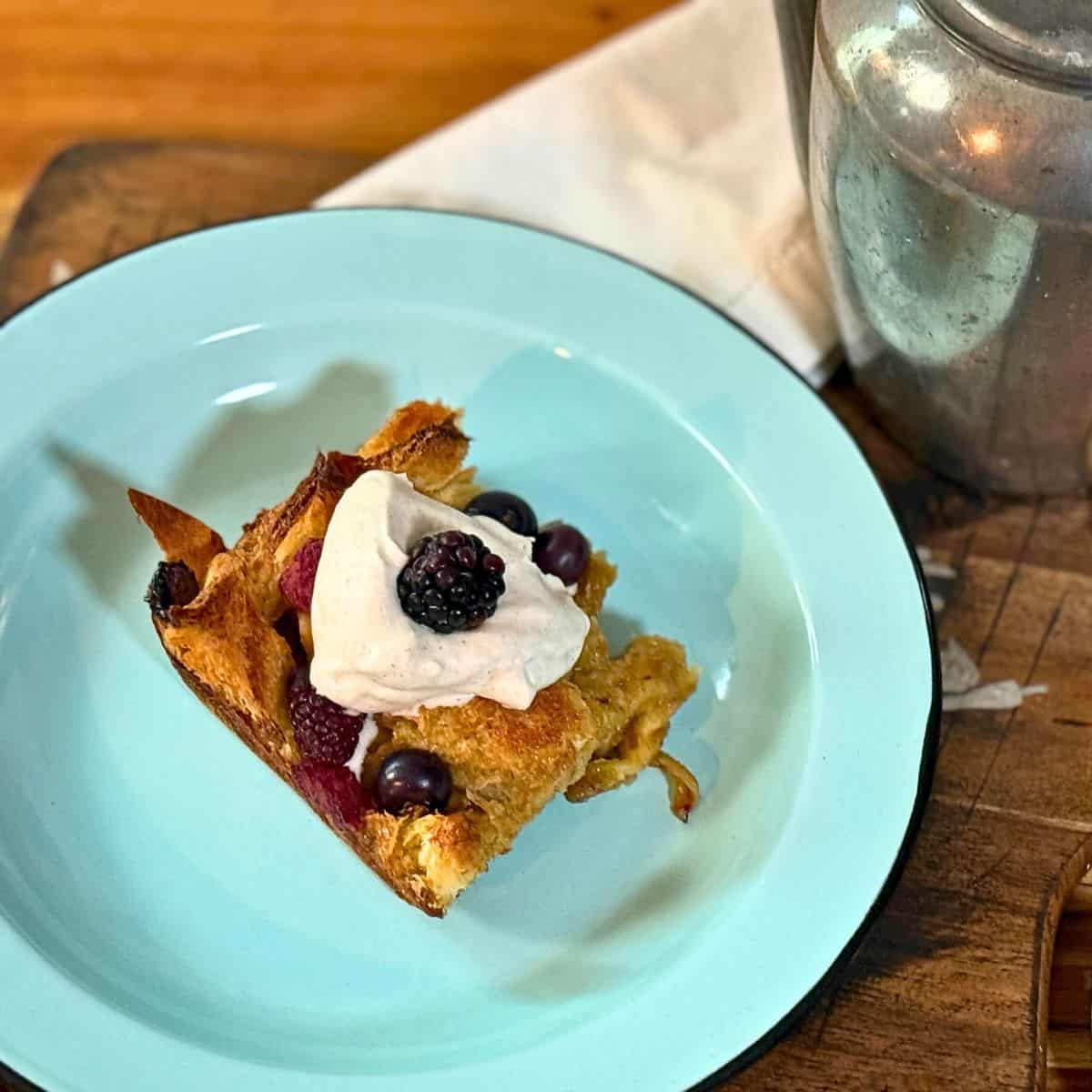 slice of french toast with berries, and whipped cream on top on a blue plate, with a white napkin