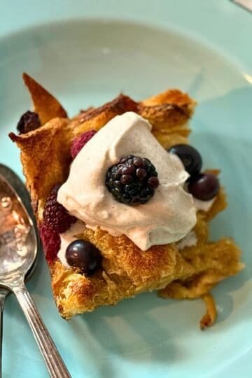 french toast on a blue plate with two spoons, whipped cream and berreis