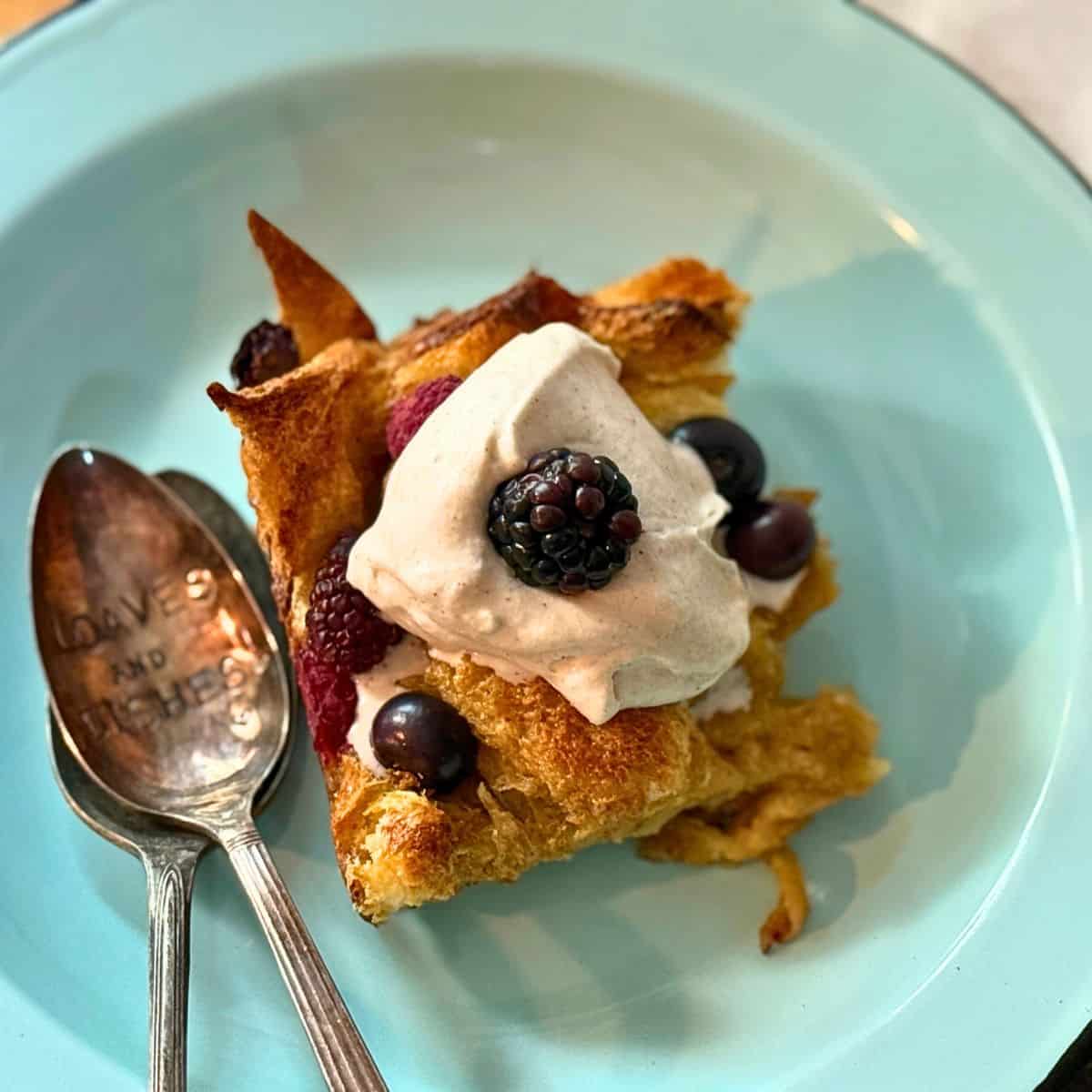french toast on a blue plate with two spoons, whipped cream and berreis