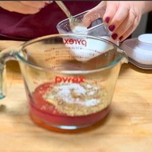 ingredients for greek dressing being added to a glass measuring cup