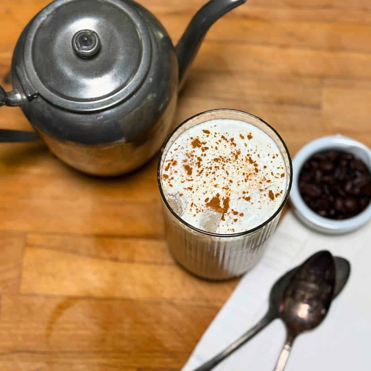 a glass of coffee with cold foam on top sprinkled with cinnamon
