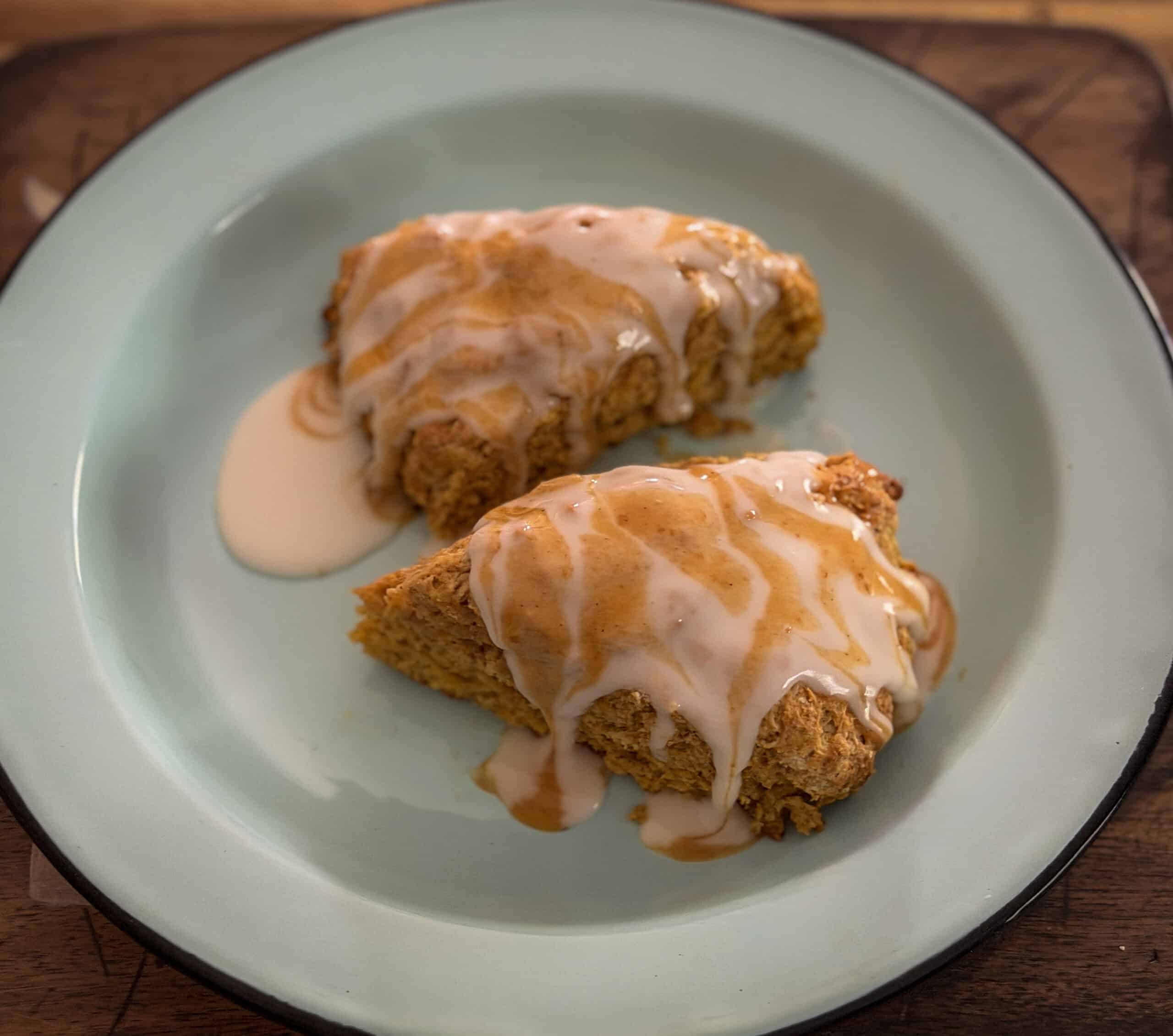Two pumpkin scones topped with vanilla and orange pumpkin spice icing served on a light blue plate.