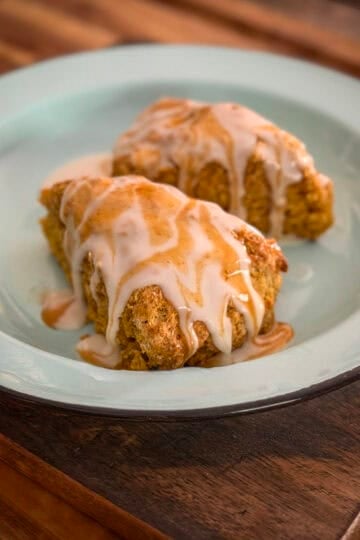 Two golden pumpkin scones covered with vanilla icing and pumpkin spice drizzle on a blue plate.