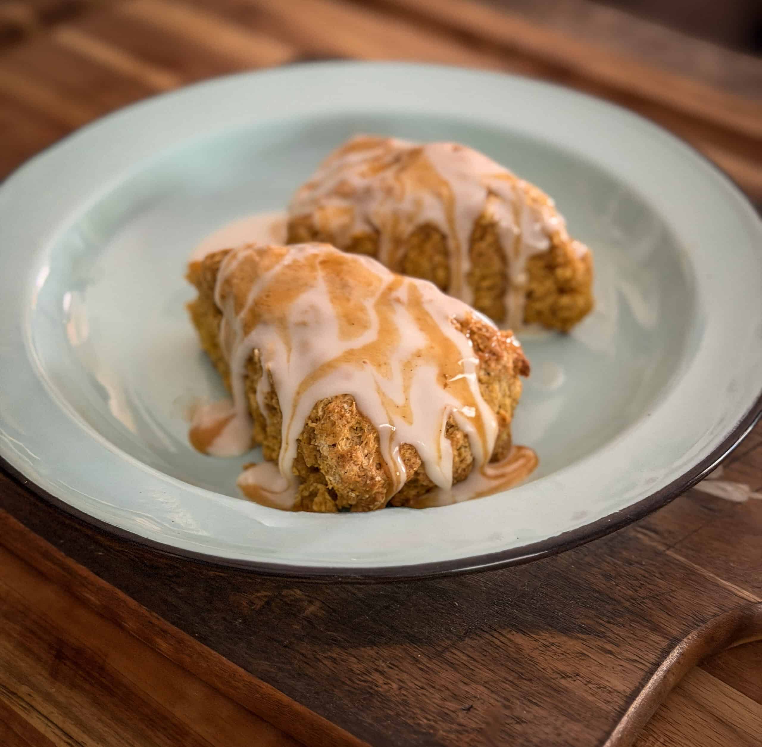 Two golden pumpkin scones covered with vanilla icing and pumpkin spice drizzle on a blue plate.