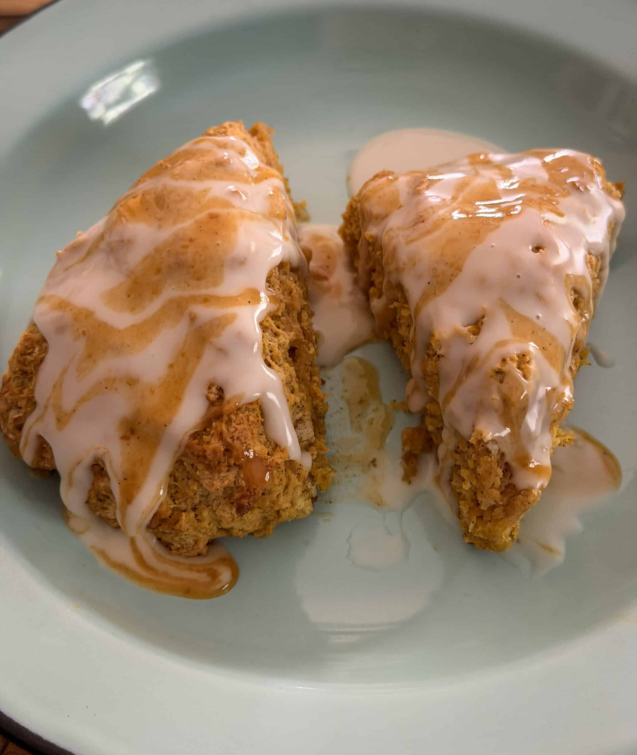 Two homemade pumpkin scones drizzled with vanilla and pumpkin spice icing on a light blue plate.