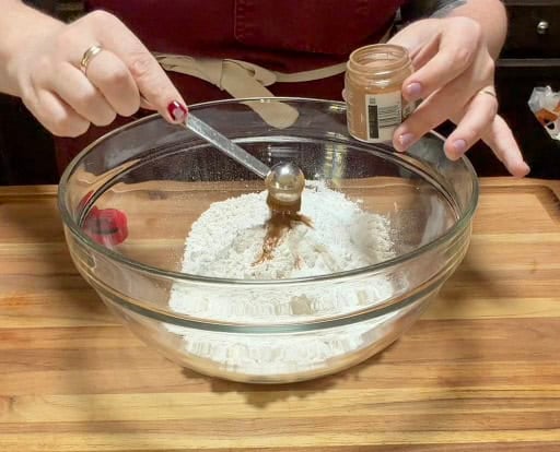 Pumpkin pie spice being measured into a bowl of flour and dry ingredients for pumpkin scones.