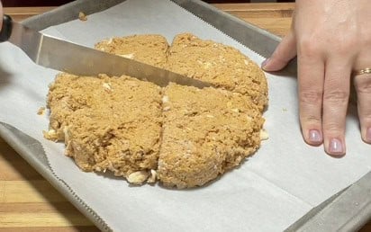 Pumpkin scone dough shaped into a round and cut into wedges on a parchment-lined baking sheet before baking.
