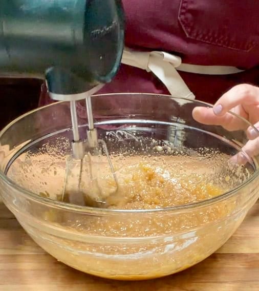Wet ingredients being mixed with a hand mixer in a glass bowl while preparing homemade brownie batter.