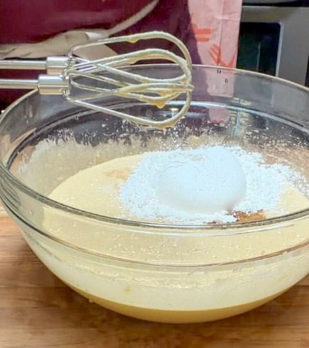 Flour and dry ingredients being added to the wet mixture while making homemade brownies.
