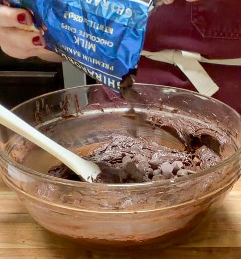 Chocolate chips being added to a bowl of rich chocolate brownie batter before baking