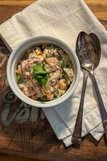 Close-up of creamy Cajun shrimp salad with shrimp, red onion, bell pepper, fresh herbs, and grainy mustard dressing in a white ramekin.